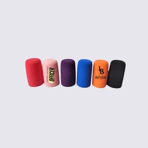 Puede incluir: Seis objetos cilíndricos de espuma en varios colores: rojo, rosa, morado, azul, naranja y negro. El objeto rosa tiene el texto "CHIEF SWAG OFFICER" y el objeto naranja tiene el texto "LB INTERNATIONAL BILLION".