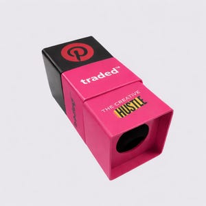May include: A pink and black box featuring the Pinterest logo and the words "traded" and "THE CREATIVE HUSTLE". The box is rectangular with a circular opening. The design is modern and eye-catching.