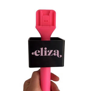 May include: A pink hair styling tool with a black holder that says "eliza."