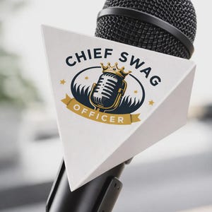 May include: A black microphone with a white triangular sign that reads "CHIEF SWAG OFFICER." The sign features a gold-crowned microphone graphic, surrounded by a navy blue oval and gold stars. The microphone is black.