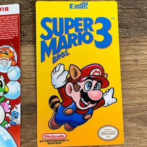 May include: A yellow Super Mario Bros. 3 game cartridge featuring Mario in a tanooki suit. The cartridge has blue text that reads "SUPER MARIO BROS." and the Nintendo logo. The official Nintendo seal is visible.