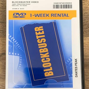 May include: A Blockbuster Video DVD case featuring the movie "Dantes Peak." The case has a blue and yellow design with the Blockbuster logo and "1-WEEK RENTAL" text. Includes store information and a barcode.
