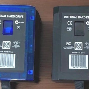 May include: Two internal hard drives are displayed. One is encased in translucent blue plastic, the other in black. Both have a black label with white text that reads "INTERNAL HARD DRIVE" and "Slim Hard Drive". Each has a barcode and model number.
