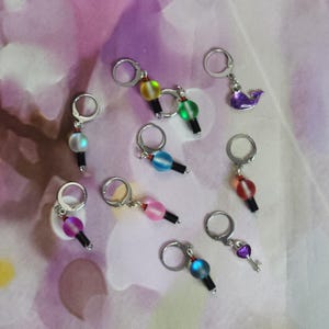 May include: A collection of handmade earrings with silver hoops. Some earrings feature colorful glass beads in various colors, while others have small charms, including a purple whale and a key.