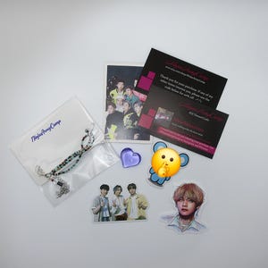May include: An assortment of items including a beaded bracelet, stickers, cards, and a purple heart-shaped object. The bracelet is in a clear plastic bag with the text "Ninja Army Camp". The stickers feature images of people.