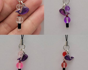 Puede incluir: Cuatro charms para teléfono con un charm de ballena morado, una cuenta transparente y una cuenta de color. Las cuentas son roja, rosa, morada y transparente.