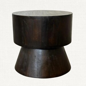 May include: A dark brown wooden stool with a cylindrical top and a conical base. The wood grain is visible, and the stool has a smooth, polished finish. The design is simple and modern, suitable for various interior styles.