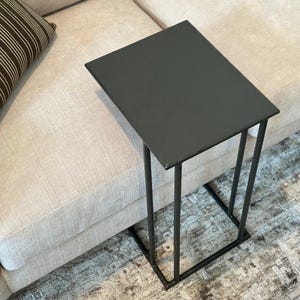 May include: A black rectangular side table with a minimalist design. The table has a flat top and a sturdy, geometric base. The table is approximately 20 inches long, 12 inches wide, and 24 inches tall.