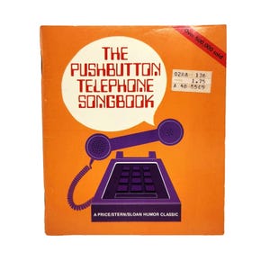May include: An orange book cover with the title "THE PUSHBUTTON TELEPHONE SONGBOOK" in red and white. A purple telephone illustration is featured. The cover also includes the text "Over 500,000 sold."