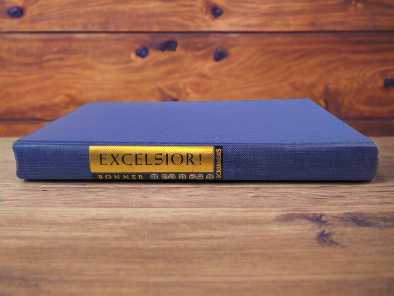 Naked book spine – Blue cloth-bound spine with bright gold title strip reading “Excelsior!” and “Scribners.”