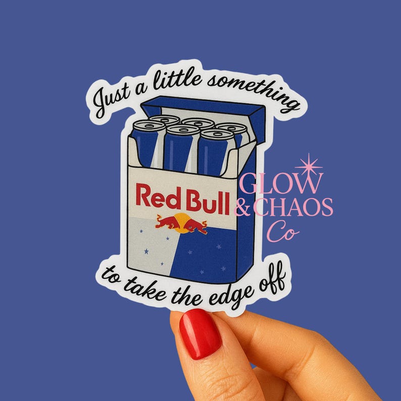 May include: A sticker featuring a cartoon illustration of a Red Bull six-pack. The box is blue and white with the Red Bull logo. Text on the sticker reads "Just a little something to take the edge off."