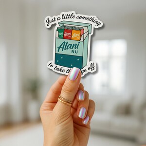 May include: A sticker featuring a cartoon illustration of a box of Alani Nu energy drinks. The box is teal with the brand name in white. The sticker has the text "Just a little something to take the edge off."