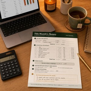 May include: A printed financial planning worksheet titled This Month's Money with handwritten entries for income, essential outgoings, and savings goals, featuring a dark green header and organized sections for tracking monthly budget data.