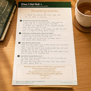 May include: A white paper financial tracker sheet with dark green headers and gold accents. The text includes sections titled What I Did Well, This month I am proud that, and numbered prompts from 2 to 5. It features handwritten notes and a bottom section with the text Managing money with an ADHD brain is genuinely hard. The sheet is placed on a wooden surface with a gold pen.