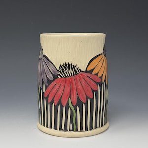 Puede incluir: Taza cilíndrica de cerámica con fondo color crema y diseño floral. Las flores son en tonos morado, rojo y naranja, sobre un patrón de rayas blancas y negras. La taza tiene una superficie texturizada.