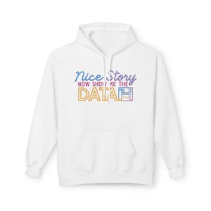 Puede incluir: Sudadera con capucha blanca con bolsillo delantero. La parte delantera presenta el texto "Nice Story, Now Show Me The Data" en degradado azul, naranja y morado. También se incluye un icono de disquete.