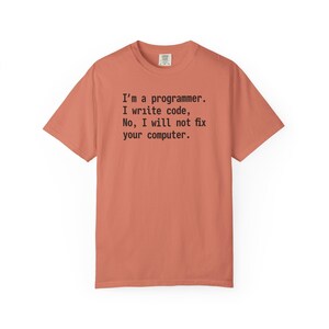 Op de afbeelding: Koraalrood T-shirt met de zwarte tekst "I'm a programmer. I write code, No, I will not fix your computer." Het T-shirt heeft korte mouwen en een ronde hals.