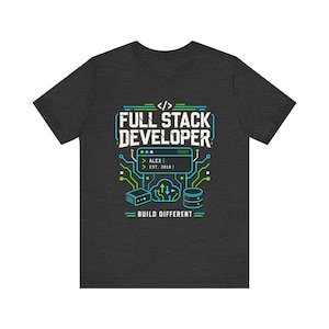 May include: A dark charcoal gray t-shirt featuring a graphic print with the text FULL STACK DEVELOPER, BUILD DIFFERENT, ALEX, and EST. 2018. The design includes white, blue, and green lines, a code bracket icon, a cloud, and server icons.