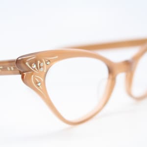 Op de afbeelding: Een vintage bril met een kattenoogvormig montuur in lichtbruin met strasssteentjes op de pootjes.