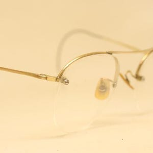 Puede incluir: Gafas de metal dorado con lentes transparentes. Las gafas tienen un diseño sin montura y un marco fino y delicado.