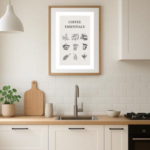 Könnte beinhalten: Ein gerahmter Druck mit der Aufschrift "COFFEE ESSENTIALS" hängt über einem Küchenbecken. Der Druck zeigt schwarz-weiße Illustrationen von Kaffeeartikeln. Die Küche hat weiße Schränke, eine Holz-Arbeitsplatte und einen Wasserhahn aus Edelstahl.