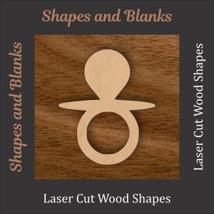 May include: A laser-cut wooden pacifier shape. The pacifier is light brown and sits on a dark brown wood grain background. The text "Shapes and Blanks" and "Laser Cut Wood Shapes" are displayed in the image.