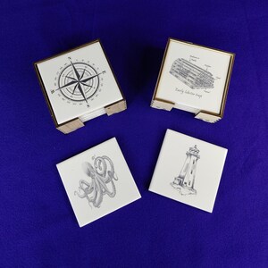 May include: Set of nautical-themed coasters. Each white ceramic tile features a black and white illustration: a compass rose, a lobster trap, an octopus, and a lighthouse. The coasters are displayed in wooden holders.