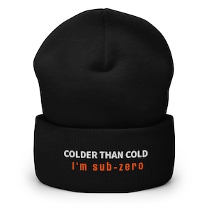 May include: Black beanie with the text "COLDER THAN COLD" in white and "I'm sub-zero" in orange. The beanie is made of a soft, knitted material. A winter accessory for cold weather.