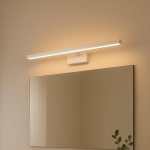 May include: A modern bathroom scene featuring a rectangular mirror with a black frame above a white countertop. A white, rectangular LED light fixture is mounted above the mirror. A black faucet and a small vase with greenery are visible.