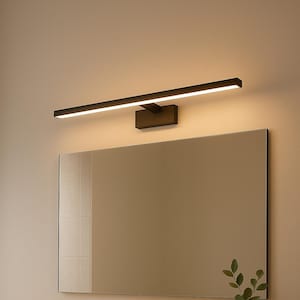 May include: A modern bathroom scene featuring a rectangular mirror above a white countertop with a built-in sink. A black faucet and a black light fixture are mounted above the mirror. A small vase with greenery and a tray with bottles add decorative touches.