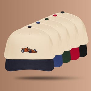 Könnte beinhalten: Eine Reihe von fünf Baseballkappen, die jeweils eine cremefarbene Krone und ein gesticktes orangefarbenes Rennauto auf der Vorderseite aufweisen. Die Schirme variieren in der Farbe, darunter Marineblau, Königsblau, Dunkelgrün, Rot und Schwarz.