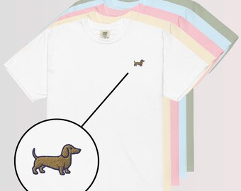 May include: White t-shirt with a small embroidered dachshund dog in brown and purple. The image shows the shirt in a variety of pastel colors, including pink, yellow, blue, and green. The dog embroidery is detailed in a close-up view.