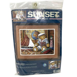 May include: Sunset Needlepoint kit titled "Bear Ahoy!" featuring a teddy bear wearing a sailor outfit, a sailboat, a globe, and a lighthouse. The kit is designed by Anna Kajewski and measures 8.3 x 10 inches.