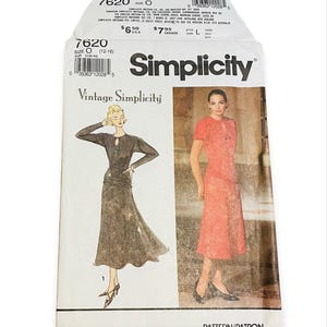 May include: A Simplicity 7620 sewing pattern envelope featuring a black long-sleeved dress with a keyhole neckline and a coral short-sleeved dress. The white paper envelope displays the brand name, pattern number, and illustrations of both garments.