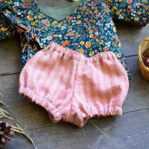 May include: A pink and white striped baby bloomer with a ruffled edge. The bloomer is made of a soft, lightweight fabric and is perfect for a baby girl.