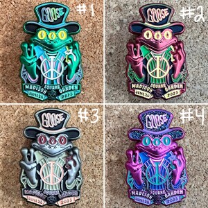 May include: Four colorful enamel pins featuring a frog design with a top hat and the word "GOOSE". Each pin has a peace sign and the text "MADISON SQUARE GARDEN JUNE 28 2025". The pins are in shades of green, red, silver, and purple.