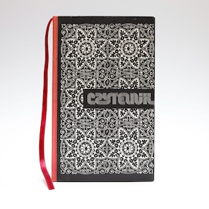 Puede incluir: Un libro de tapa dura en blanco y negro con un patrón floral repetitivo en la cubierta. La palabra CZYTANKA está impresa en una fuente estilizada en el centro. Un marcador de cinta roja fina sobresale del lomo del libro.