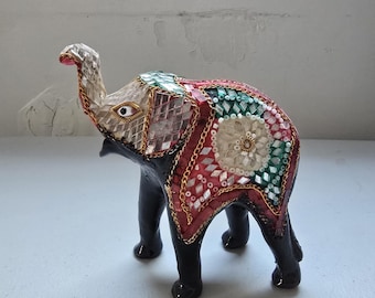 May include: Decorative elephant figurine with a black body and legs. The elephant's head is silver and pink, and its back is adorned with red, green, and white mosaic tiles, outlined with gold-colored chain. A unique home decor item.