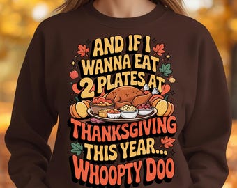 May include: A brown sweatshirt with a Thanksgiving-themed graphic. The graphic includes a roasted turkey, side dishes, pumpkins, and the text "AND IF I WANNA EAT 2 PLATES AT THANKSGIVING THIS YEAR... WHOOPTY DOO."