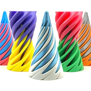 以下が含まれることがあります： カラフルな円錐形の装飾品5つのコレクション。各オブジェクトは、青、ピンク、黄色、緑、オレンジなど、異なる配色を持つスパイラルデザインが特徴です。白い表面に配置されています。