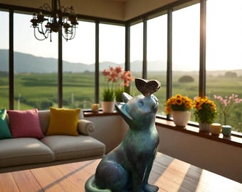 Puede incluir: Una estatua de gato de color verde azulado con una mariposa en la cabeza. El gato está sentado en una mesa de madera frente a una gran ventana. La habitación tiene un sofá con cojines coloridos y plantas en macetas.