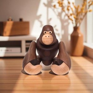 May include: A wooden gorilla figurine with a dark brown body and light brown face and hands. The gorilla has a simple, stylized design, with rounded features and a playful expression. The figurine is sitting on a wooden surface.