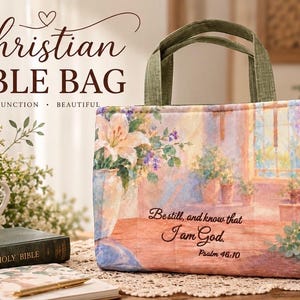 May include: A rectangular fabric tote bag with olive green handles featuring a printed watercolor scene of a room with lilies and a candle. The text "Be still, and know that I am God. Psalm 46:10" is printed in black script on the front of the bag.
