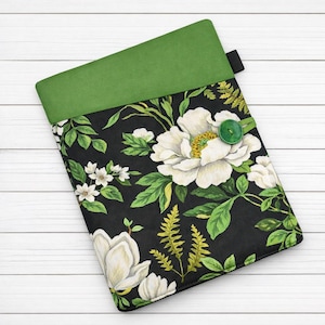 May include: A black floral book sleeve featuring white peony flowers and green foliage. The top section is a solid green, with a green button closure. Designed to protect books and e-readers.