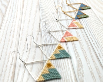 May include: Four pairs of geometric triangle earrings with beaded designs in shades of blue, pink, beige, and brown. The earrings are made with silver-toned hooks.