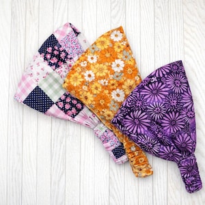 May include: Three fabric headbands with elasticated backs. One features a patchwork design with pink floral, navy polka dot, and green gingham patterns. Another is orange with white and yellow flowers. The third is purple with a floral design.