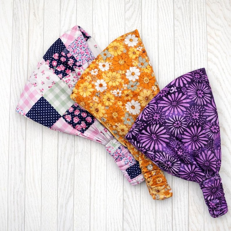 May include: Three fabric headbands with elastic backs. One is patchwork with pink floral, navy polka dot, and green gingham patterns. The second is orange with white and yellow flowers. The third is purple with a floral design.