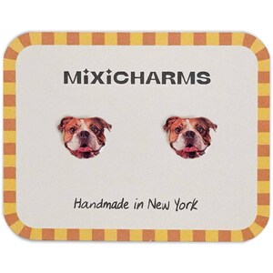 May include: A pair of stud earrings featuring a bulldog face design. The earrings are displayed on a white card with the text "MixiCharms" and "Handmade in New York". The card has a yellow and brown checkered border.