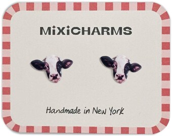 May include: A pair of cow head stud earrings on a cream-colored card with a red and white checkered border. The card reads "MixiCharms" and "Handmade in New York". The earrings feature black and white cow faces.