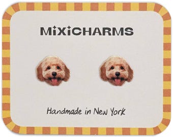 Può includere: Un paio di orecchini a bottone MixiCharms con facce di cane sorridenti e lingue rosa. Sono presentati su una carta bianca con la scritta "MixiCharms" e "Handmade in New York". La carta ha un bordo giallo e arancione.